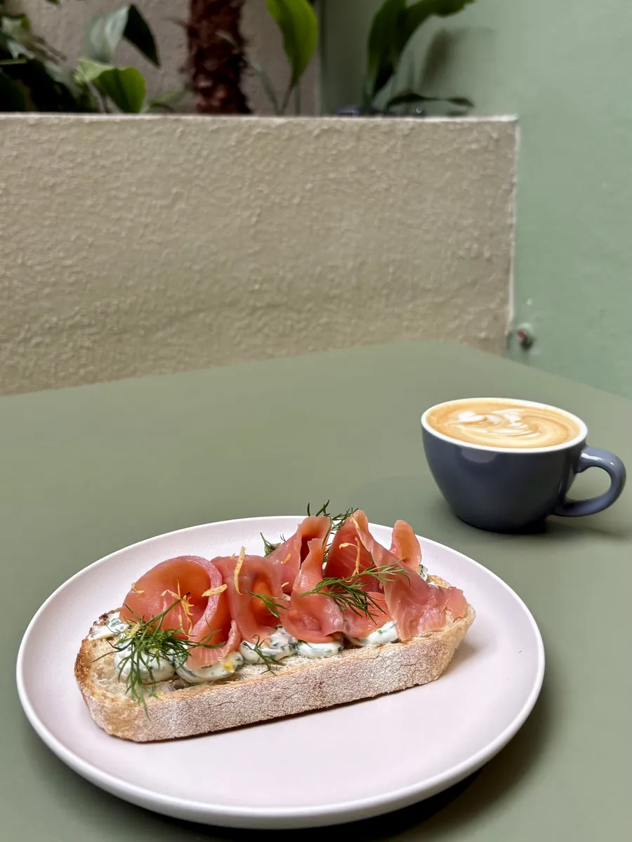 Tostada con salmón y un café en el patio, con la palmera y el cantero de fondo