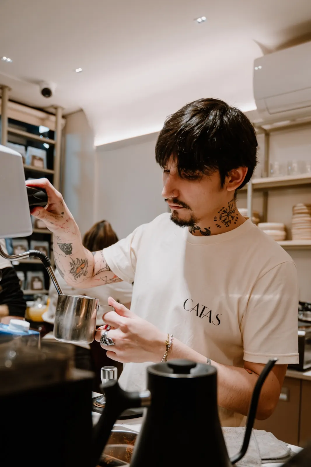Un barista con remera de CATAS espuma leche detrás de la barra