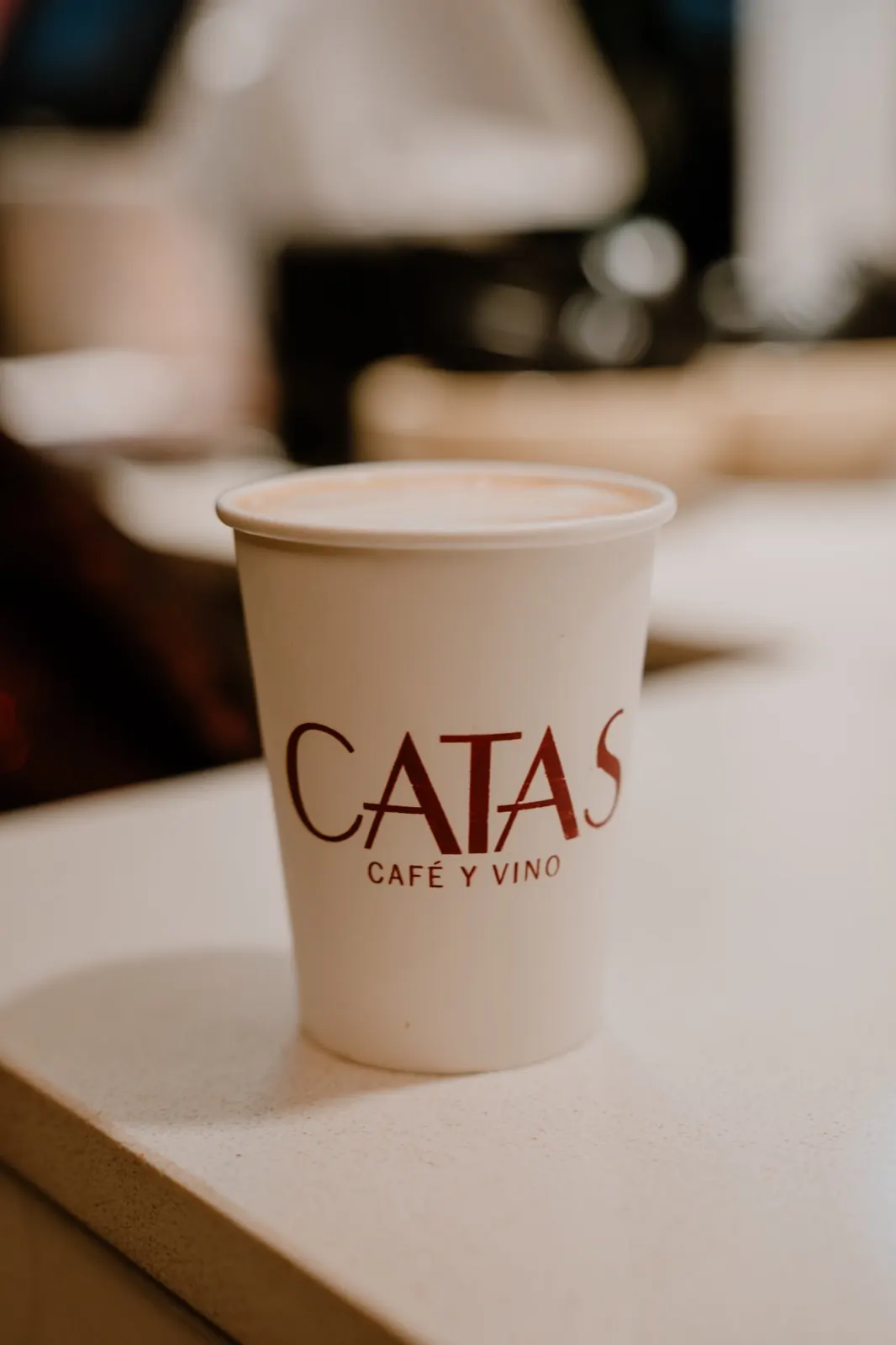 Un vaso de café para llevar con el logo de CATAS Café y Vino, sobre la barra