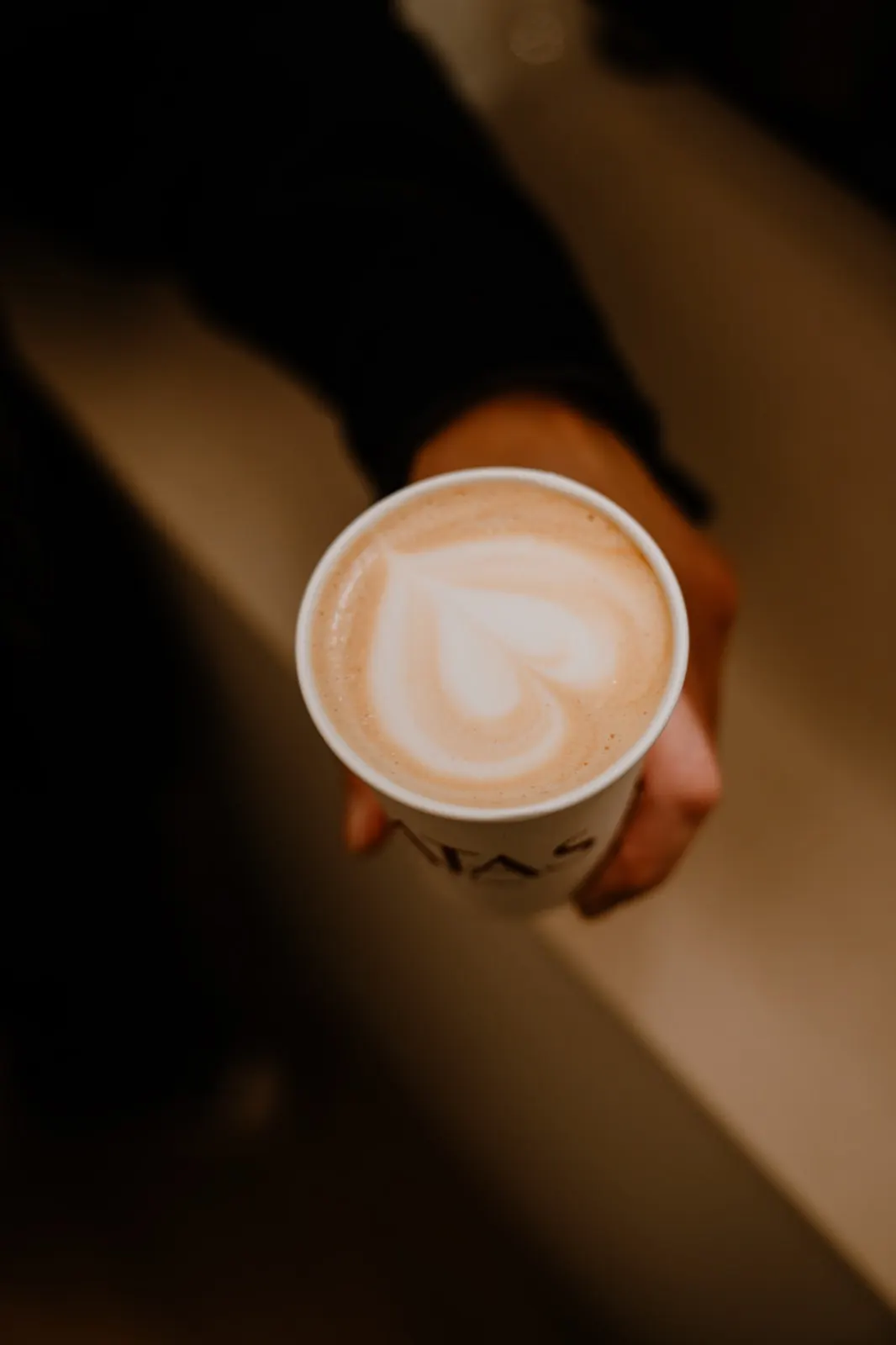 Una mano sostiene un latte con un corazón dibujado en la espuma