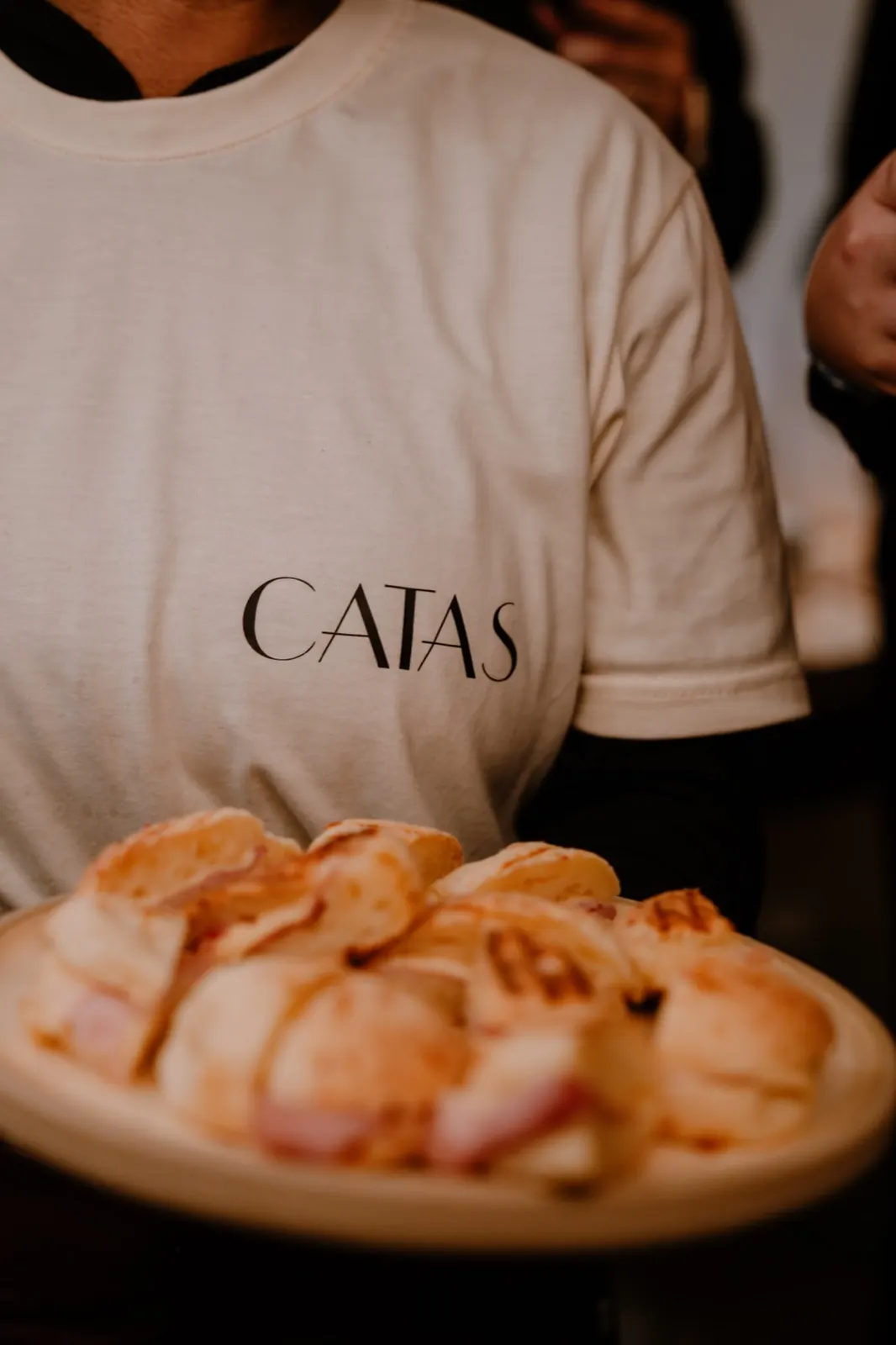 Una persona del equipo, con remera de CATAS, lleva un plato de panificados rellenos