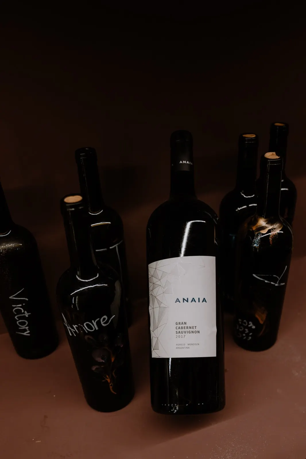 Una botella de Anaia entre botellas oscuras escritas a mano con tiza