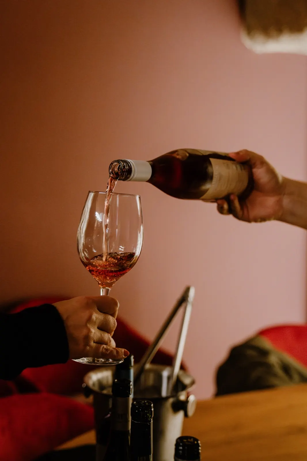Alguien sirve vino rosado en una copa, junto a una frapera con botellas