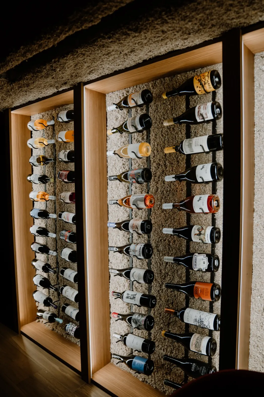 La pared de botellas de la cava: marcos de madera iluminados con las botellas acostadas, una sobre otra